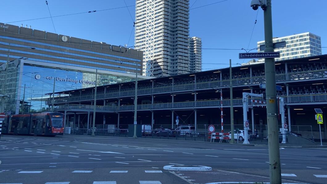 Een foto van Den Haag Centraal, met rechts de fietsflat en op de voorgrond een straatnaambordje met 'schedeldoekshaven'