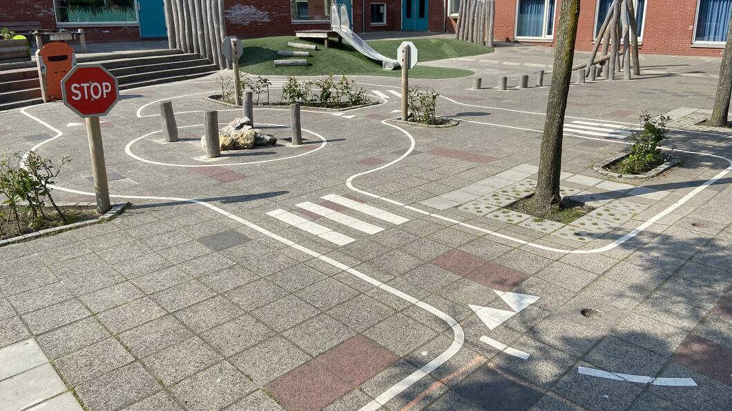 een foto van een schoolplein waar op de tegels een stratennetwerk is getekend, compleet met een stopbord. 