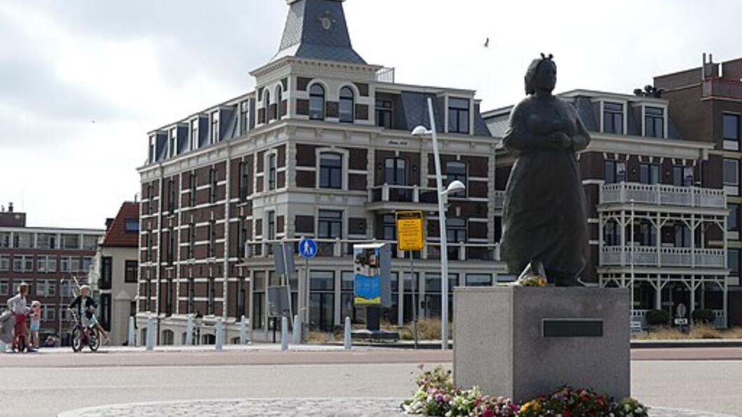 Vissersvrouw van Scheveningen met op de achtergrond bebouwing 