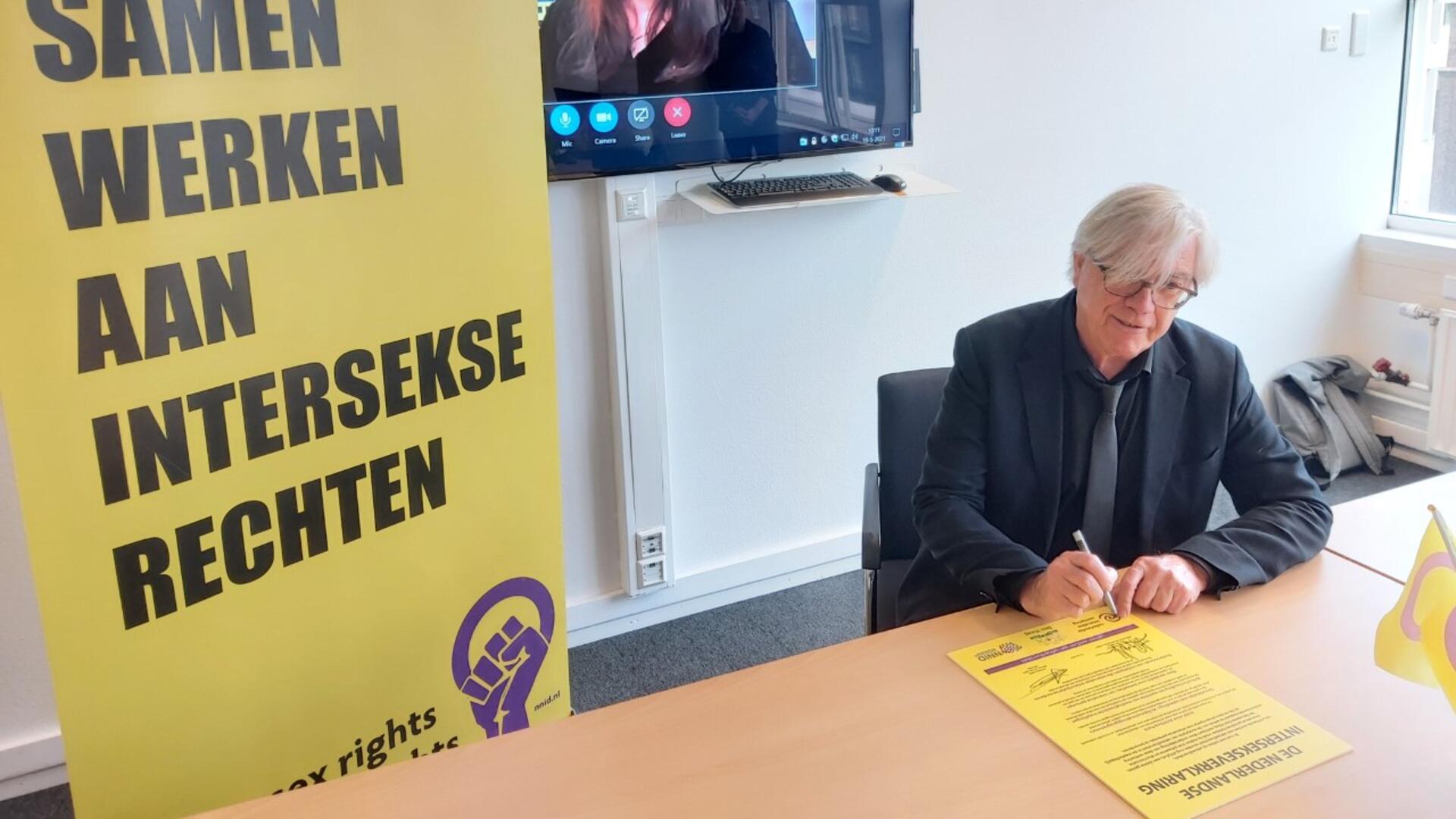 een foto van Bert van Alphen die de intersekseverklaring tekent. 