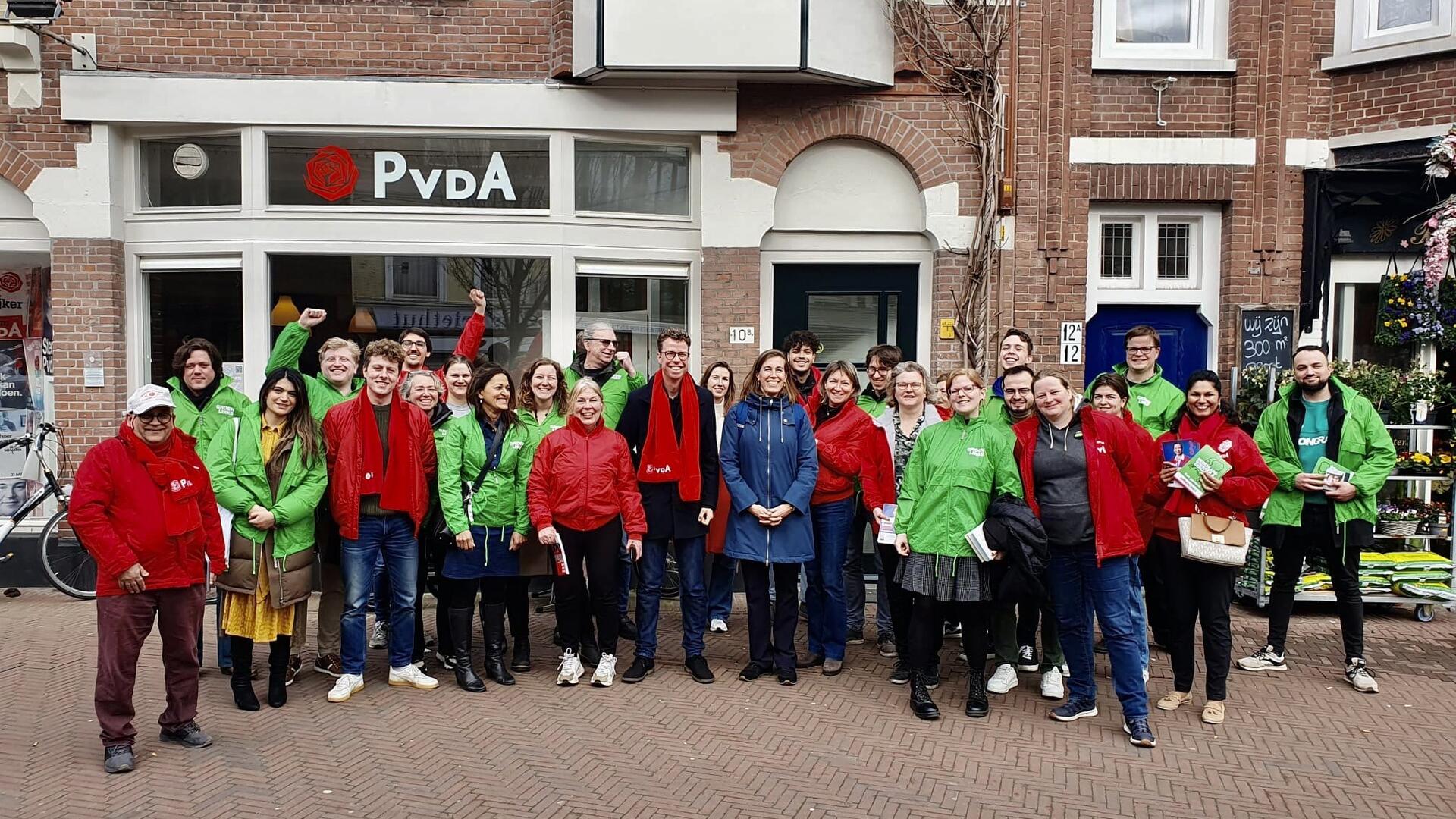 Een groep PvdA- en GroenLinks-leden poseren samen in hun rode en groene campagnejasjes voor het pand van de PvdA Den Haag.